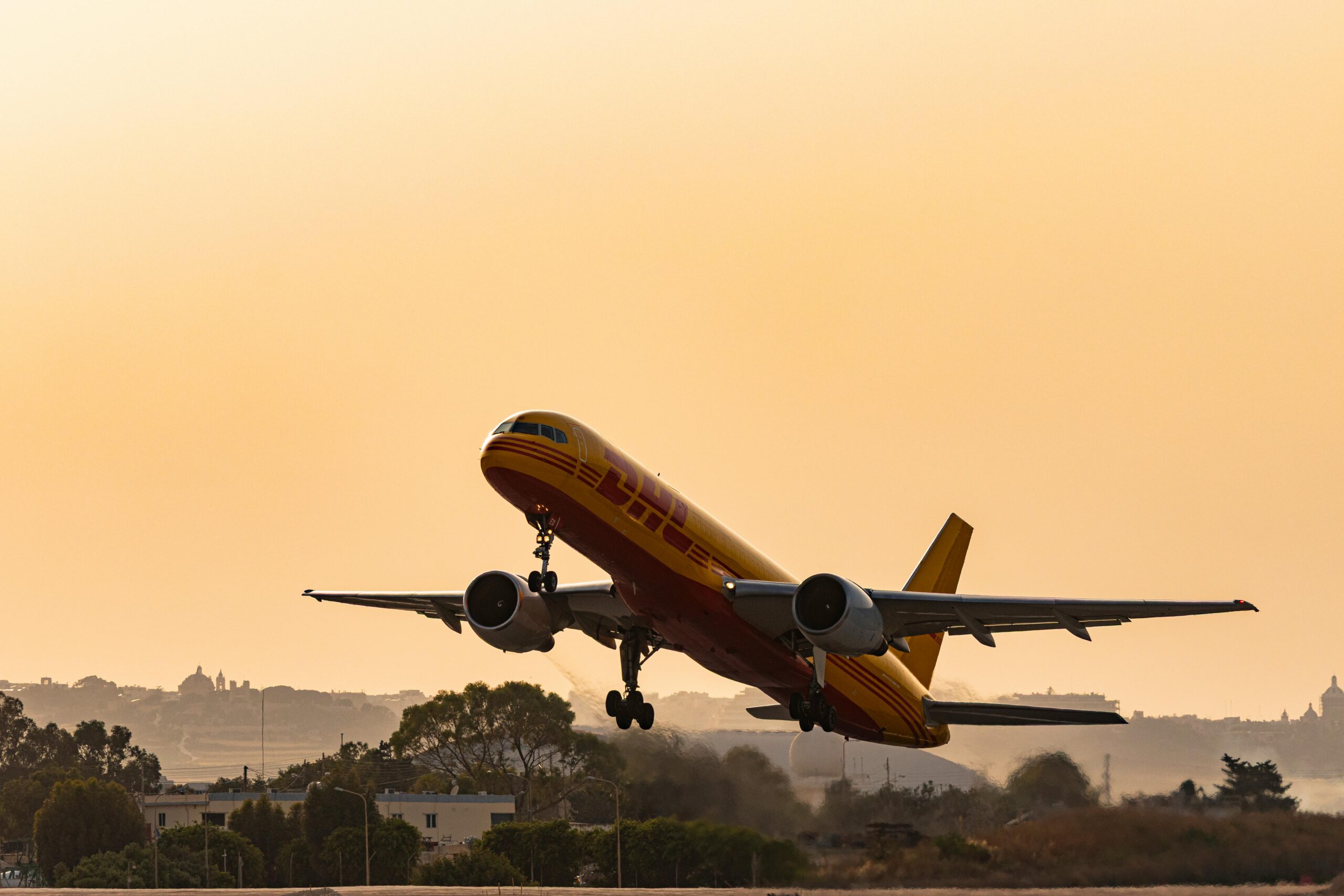 A DHL cargo plane takes off against a golden sunset sky, showcasing aviation in action.